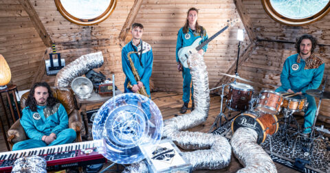 4 musiciens posent avec leurs instruments dans une pièce en bois.