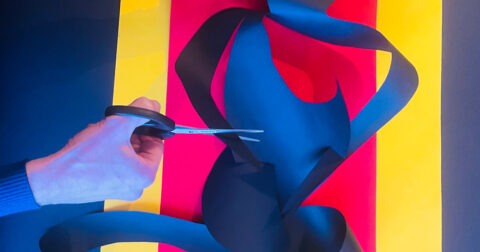 un comédien découpe aux ciseaux du papier coloré pur créer une forme