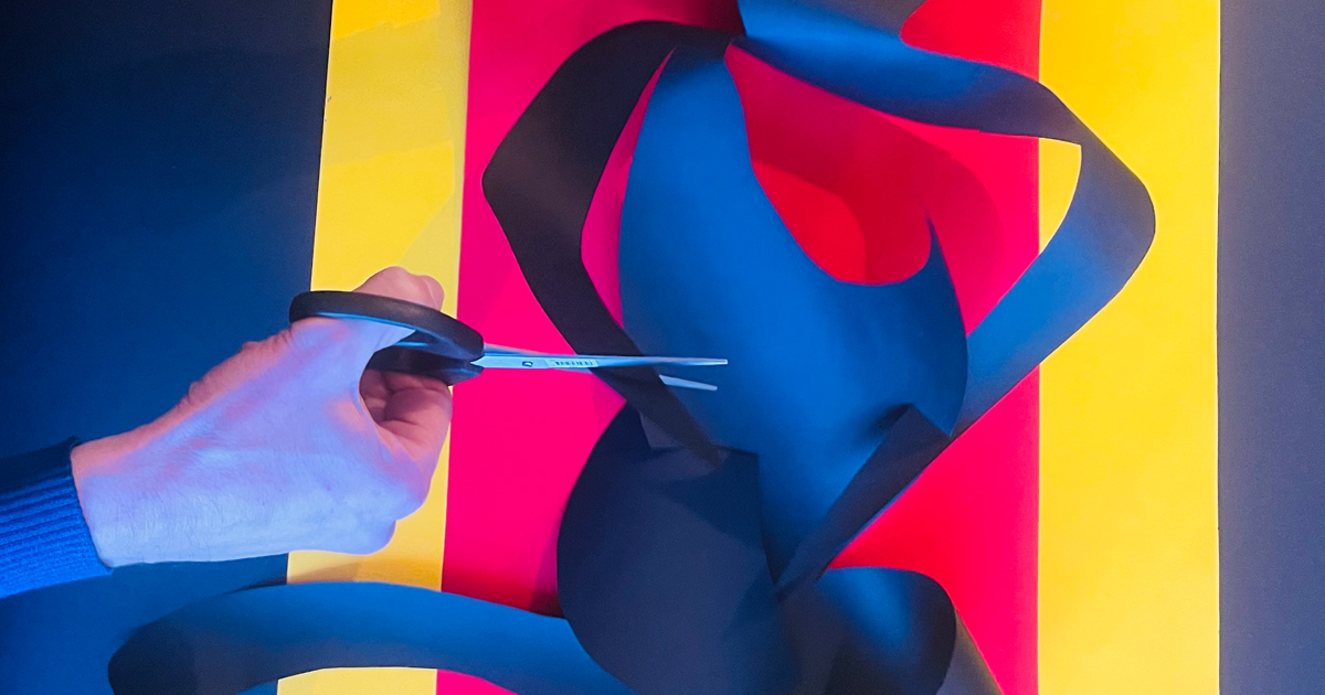 un comédien découpe aux ciseaux du papier coloré pur créer une forme